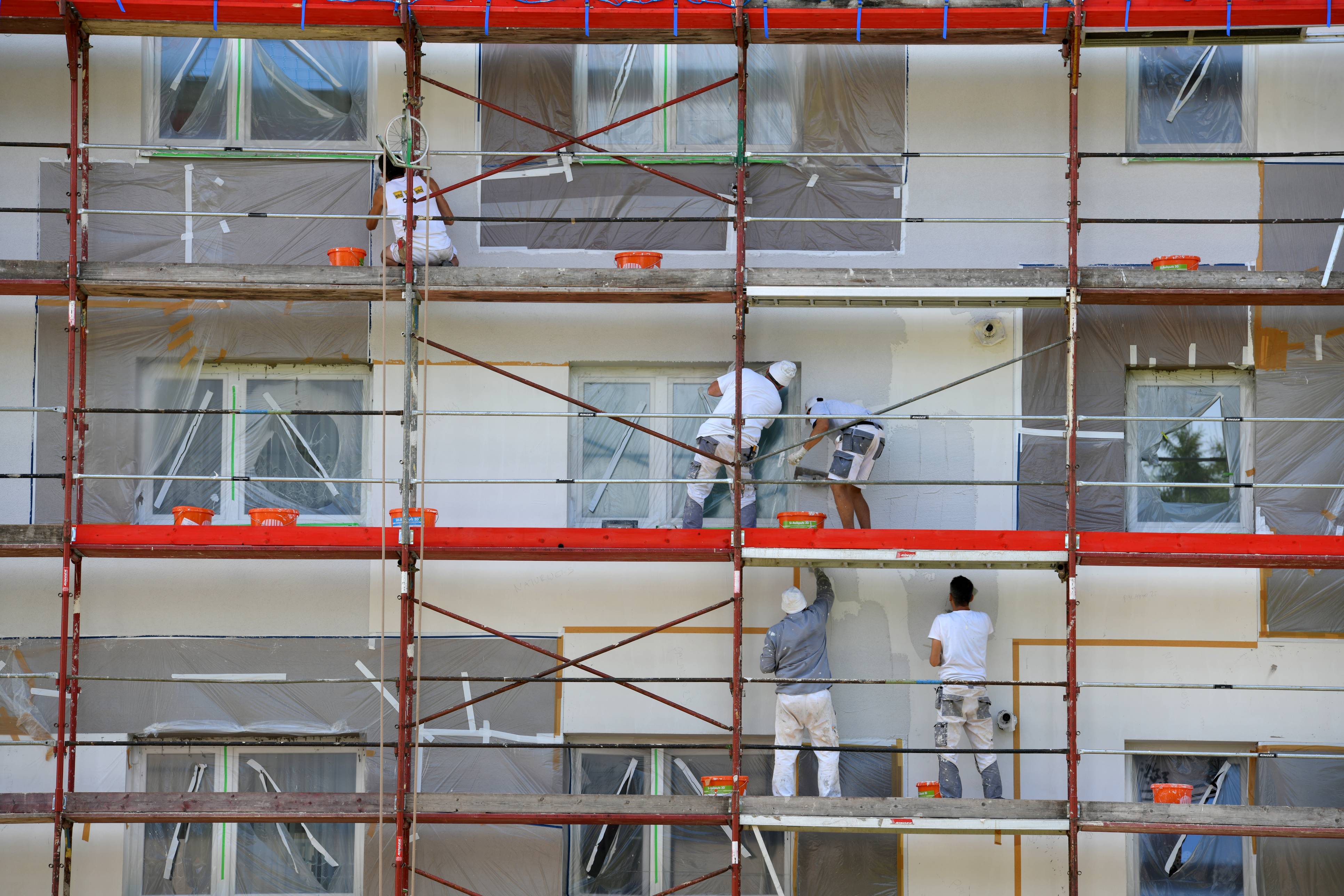 Vista parcial de la fachada de un edificio, sobre un andamio varios obreros realizan labores de rehabilitación